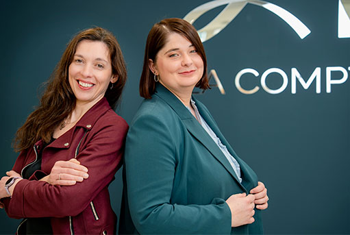 Portrait de Adrianna et Julianne, consultantes, posant devant le logo de leur cabinet.
